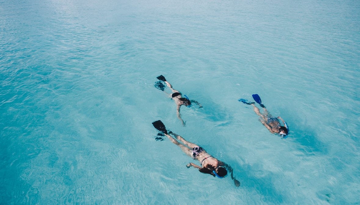 three-people-snorkelling-in-light-blue-shallow-water-view-from-above